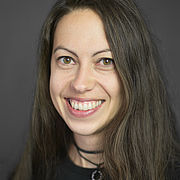 Eine junge Frau mit langen durnkelblonden Haaren und dunkelm Oberteil lächelt freundlich und aufgeschlossen.